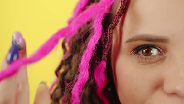 Young Woman Twisting Pink Hair and Looking at Camera on Yellow Background