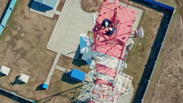 Two Industrial Climbers in Helmets and Gear Repair Lighting Lamps on Communication Mast