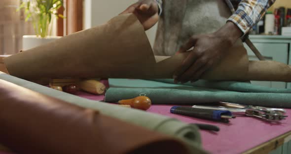 Hands of african american craftsman in apron unrolling leather in leather workshop
