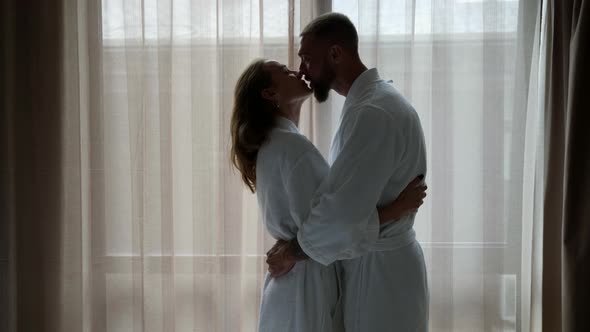 Loving Man and Woman are Hugging in Morning in Bedroom Against Window