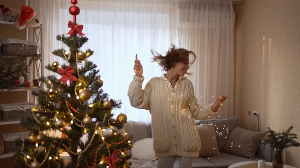 Slow Motion of Happy Pretty Woman Dancing with Christmas Lights at Cozy Festive Home with Christmas