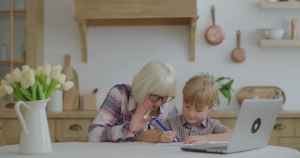 60s Grandmother Making Online Homework with Preschool Grandson at Home. Senior Woman in Glasses and