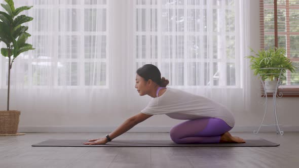 Asian woman working out in sportswear while doing yoga, seated in Child exercise, Balasana stance.