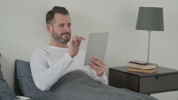Man Celebrating Success on Tablet in Bed