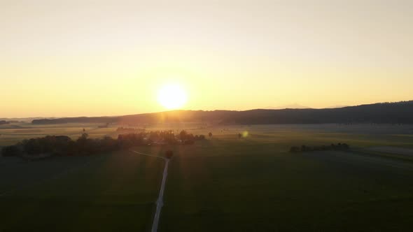 Aerial clip of the Bavarian plain during sunrise. Direct backlight from the sun and a road in the mi