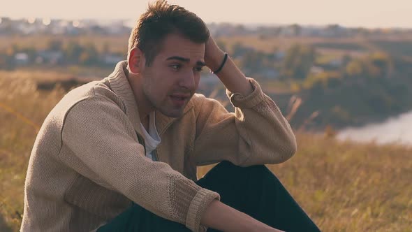 Sad Man in Warm Pullover Sits on Meadow Lit By Autumn Sun