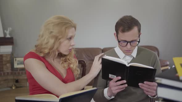 Young Modestly Dressed Man in Glasses and Curly Blond Woman Reading the Book Sitting on the Sofa