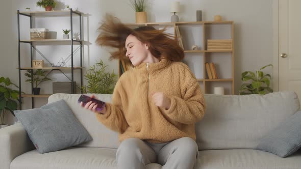 Young Caucasian Woman With Phone Sitting In Couch In Bright Room At Home Listening Favorite Music