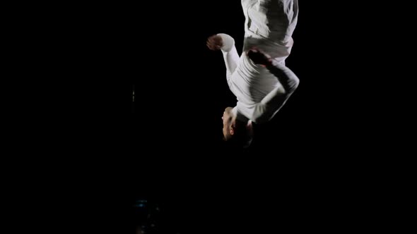 Handsome Male Professional Gymnast in White Clothes on a Black Background Performs at the Gymnastics