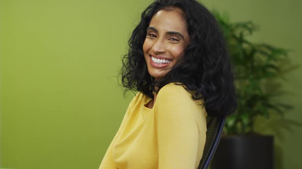 Video of happy biracial woman looking at camera on green background