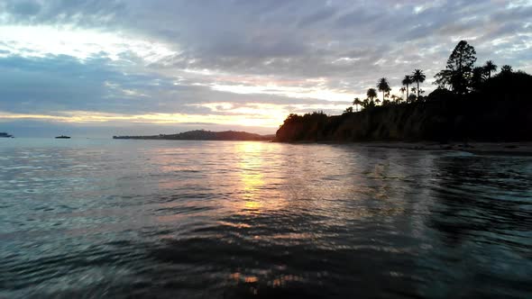 Aerial drone shot at sunset flying low over the water and reflections of the Pacific Ocean surface w