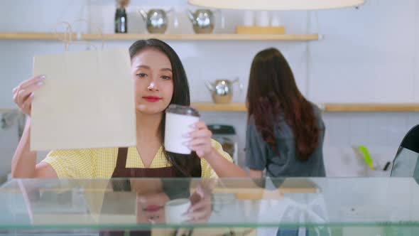 Attractive asian female cafe worker  giving takeaway food bag to customer