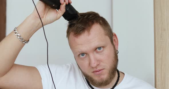 Handsome man in white t-shirts cutting hair personally himself with machine trimmer, clipper at home