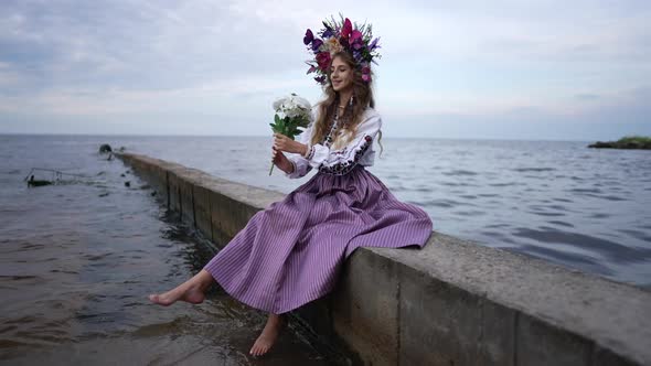 Young Ukrainian Smiling Woman with Bouquet of White Roses Sitting on River Pier Looking at Camera