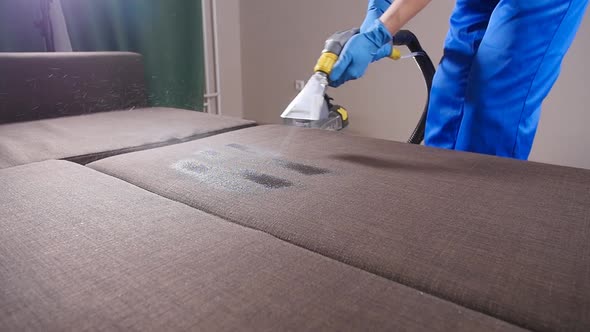 Concept of Cleaning in the Apartment and Office. Dry Cleaning Worker Removing Dirt From Sofa Indoors