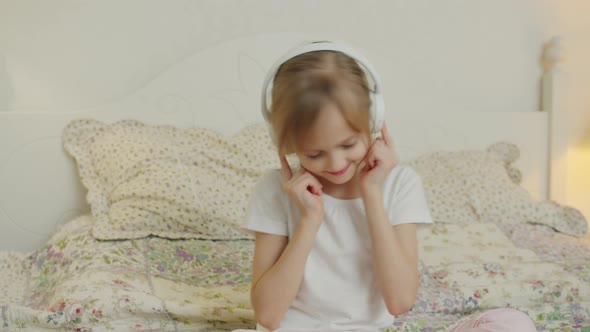 Happy Kid Enjoying Music in Headphones Moving Head Relaxing on Bed in Apartment