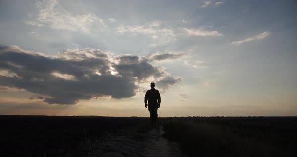 A Soldier Walks Across a Field at Sunset and Looks Around Silhouette