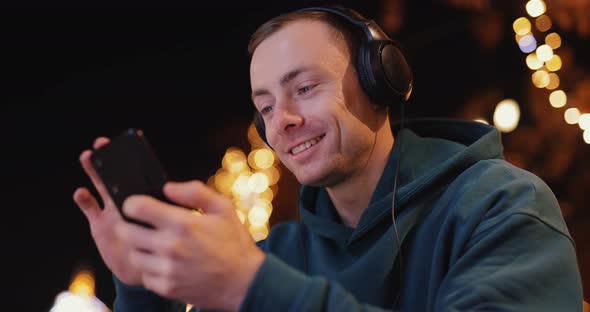 Smiling Man Using Phone in Headphones in Evening City