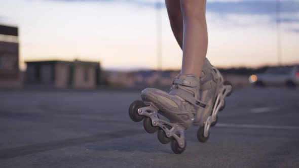 Slim Female Legs in Roller Skates Riding at Dusk on Empty Parking Lot. Unrecognizable Young