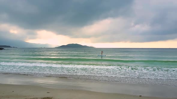 Foamy Waves Roll on Beach and Girl on Paddleboard in Ocean