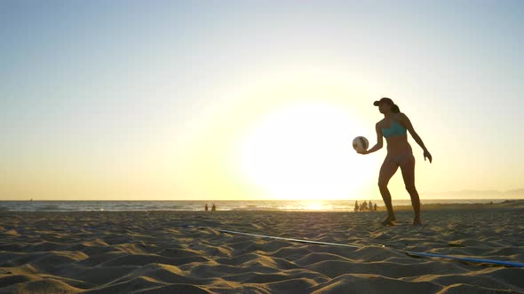 Women players play beach volleyball and a player jump serves serving the ball.
