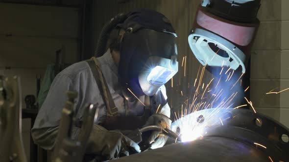 Sparks fly as a man welds a large pipe in an industrial machine shop