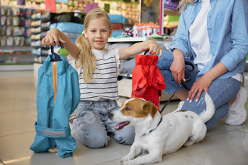 Portrait of little girl showing new clothes for dog during shopping at pet store