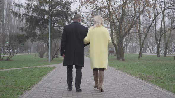 Back View of Stylish Caucasian Couple Walking Along the Alley and Talking