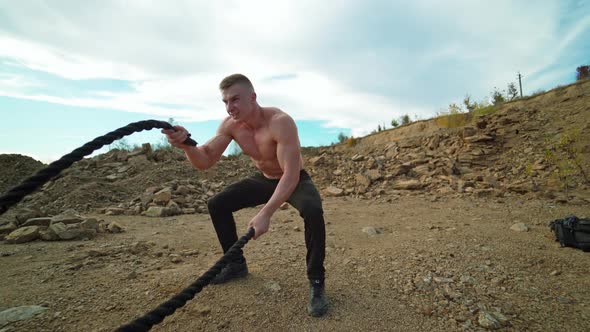 Athlete doing battle rope workout. Muscular young man working out with battling ropes