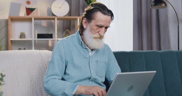 Senior Bearded Man Working on Laptop at Home and Looking at Camera with Thumb Up