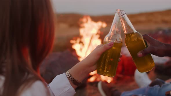 Man and Woman are Sitting Near Campfire and Clinking Cocktail Bottles Back View Closeup of Bottles