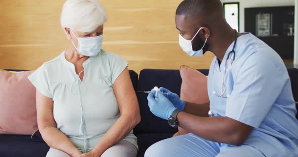 Video of african american male doctor in face mask vaccinating caucasian senior woman