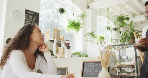 Happy african american male barista serving coffee biracial female client at cafe