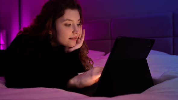Young ginger hair girl browsing her tablet at night in the bedroom