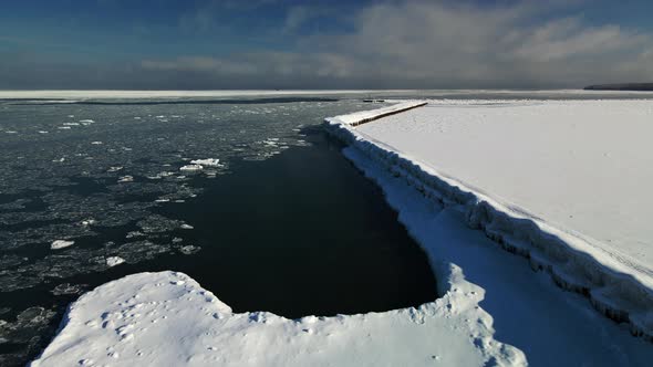 Drone footage along snow covered pier and ice chunks on Lake Huron in winter