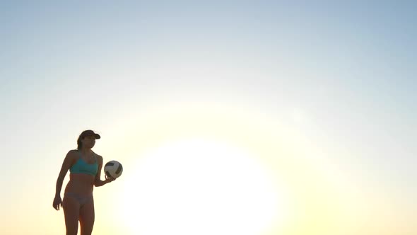 Women players play beach volleyball and a player serves the ball.