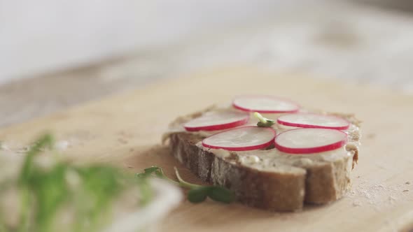 cooking sandwich on board. Slice of bread with bran, soft cheese cheese, fresh radish, microgreens