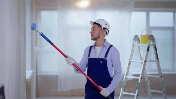 Male House Painter in Work Suit and Safety Helmet Makes Repairs Indoors and Paints Walls Using