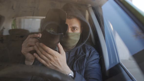 A Man in a Black Hoodie and a Protective Medical Mask on His Face Sitting Behind the Wheel of a Car