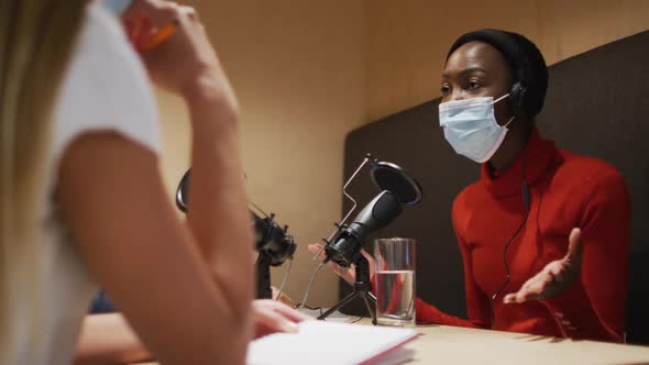 Three diverse female radio hosts wearing face masks talking on microphone for radio podcast