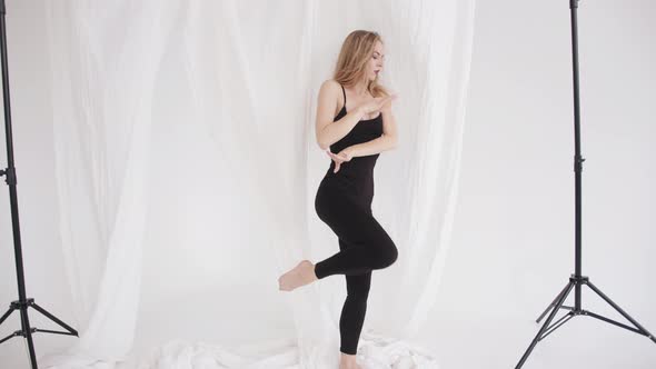 A Beautiful Young Girl in a Black Tightfitting Jumpsuit is Engaged in Stretching and Moves Like in a