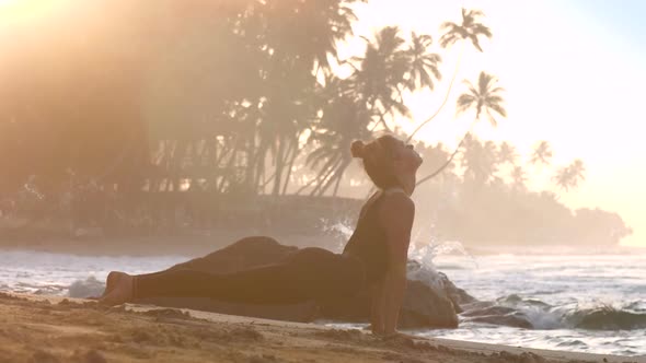 Girl Practices Yoga at Blue Waves Rolling on Stones Foaming