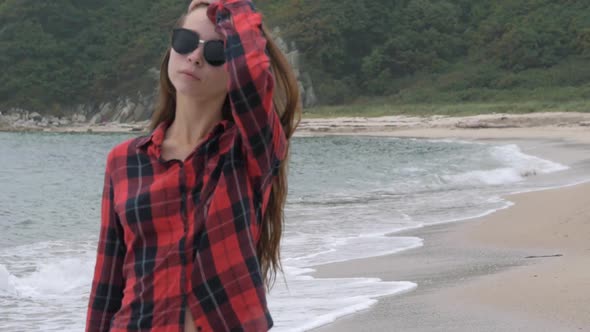 Young Beautiful European Girl Dressed in Checkered Shirt Walking on the Sand Beach Along the Sea on