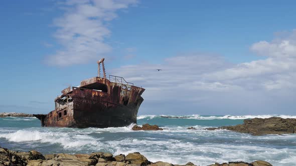 Old weathered shipwreck in shallows with waves running in, rocky coastline of L'Agulhas, South Afric