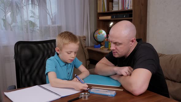 A Kind Caring Father Helps His Son to Do Homework at Home at the Table