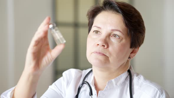 Closeup Portrait of Serious Female Doctor Holding Vaccine Jar and Looking at Camera