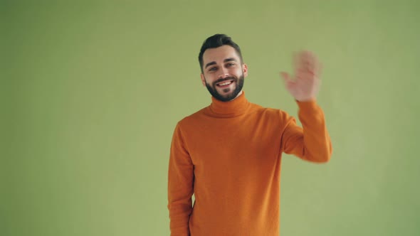 Portrait of Friendly Young Man Waving Hand and Looking at Camera with Happy Face