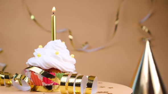 Birthday Cake or Cupcake with a Burning Golden Candle on a Beige Background