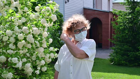 Happy Old Woman Takes Off the Mask and Sniffs a Blossoming Apple Tree