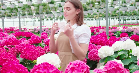 Smiling Woman Sniffing Flowers in Modern Greenhouse